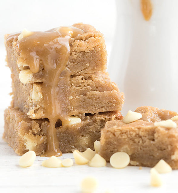 A stack of keto blondies with white chocolate chips and a drizzle of salted caramel sauce dripping down the side of the stack.