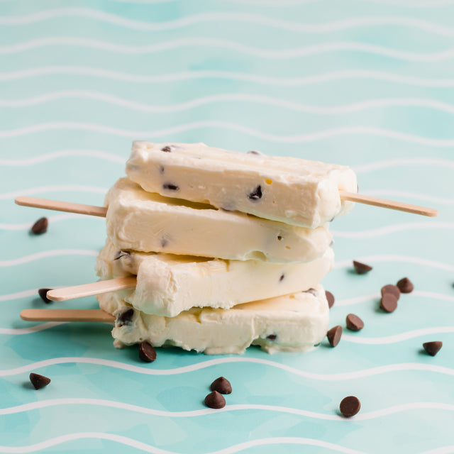 A stack of keto chocolate chip yogurt pops on a blue background surrounded by sugar free chocolate chips