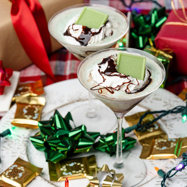 Two martini glasses filled with keto grasshopper martini and topped with a ChocZero white chocolate peppermint square